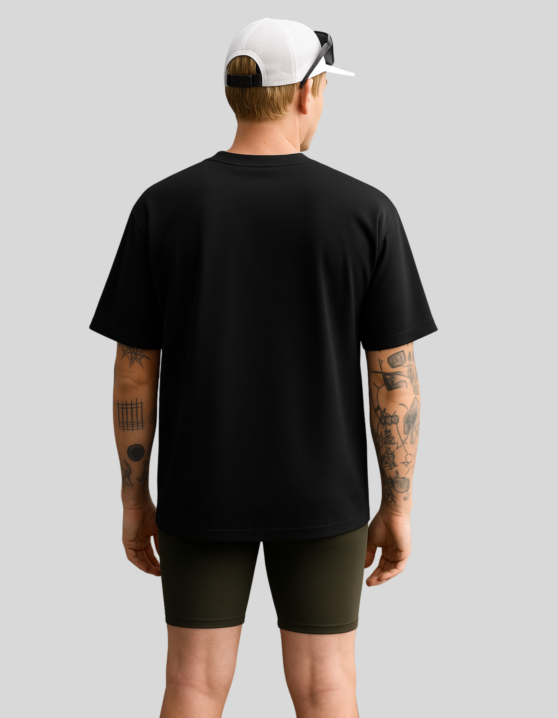 Person wearing a black t-shirt and green shorts with a white cap on a gray background